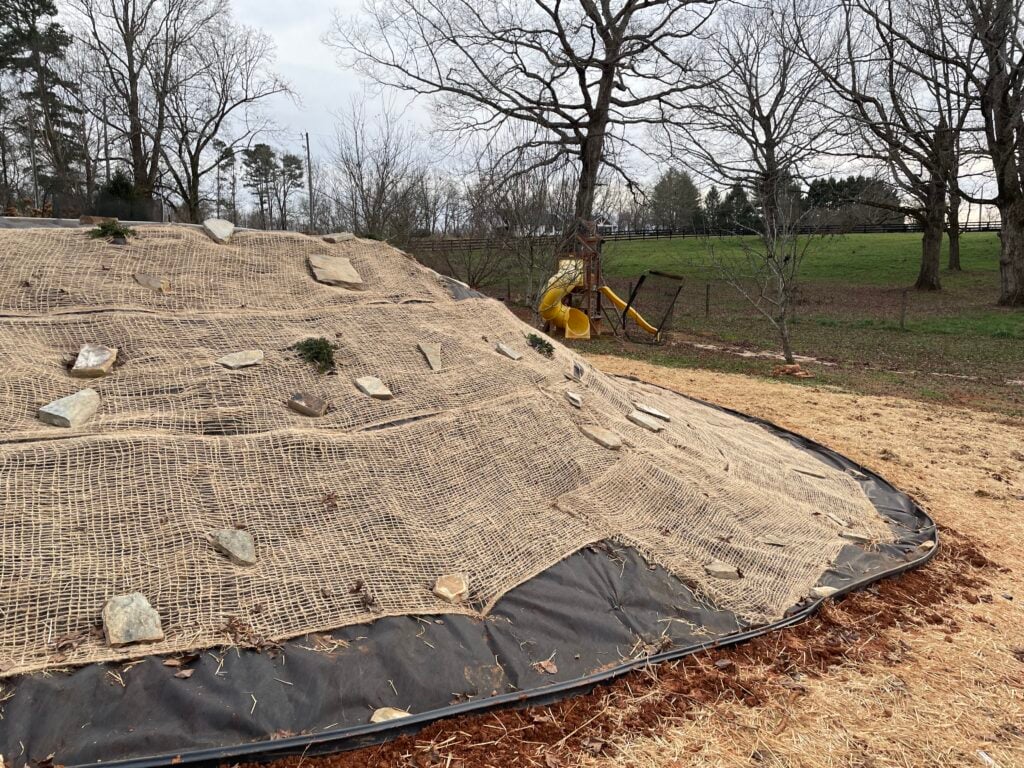 A steep bank covered with weed barrier, jute netting, and several juniper plants.