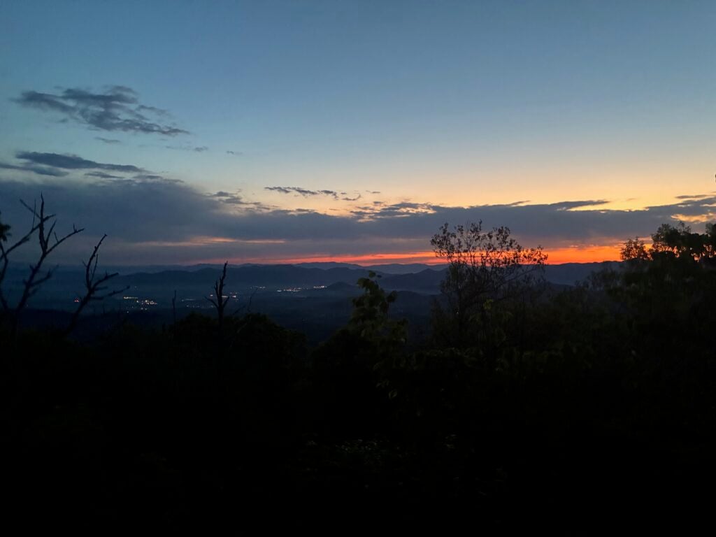 Long distance view with mountains and the beginning of the sunrise. It's still dark but the sky has brightened and there's an orange layer on the horizon.